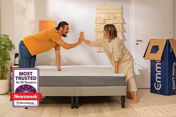 A man and a woman high fiving over an Emma mattress with an Emma box in the background.